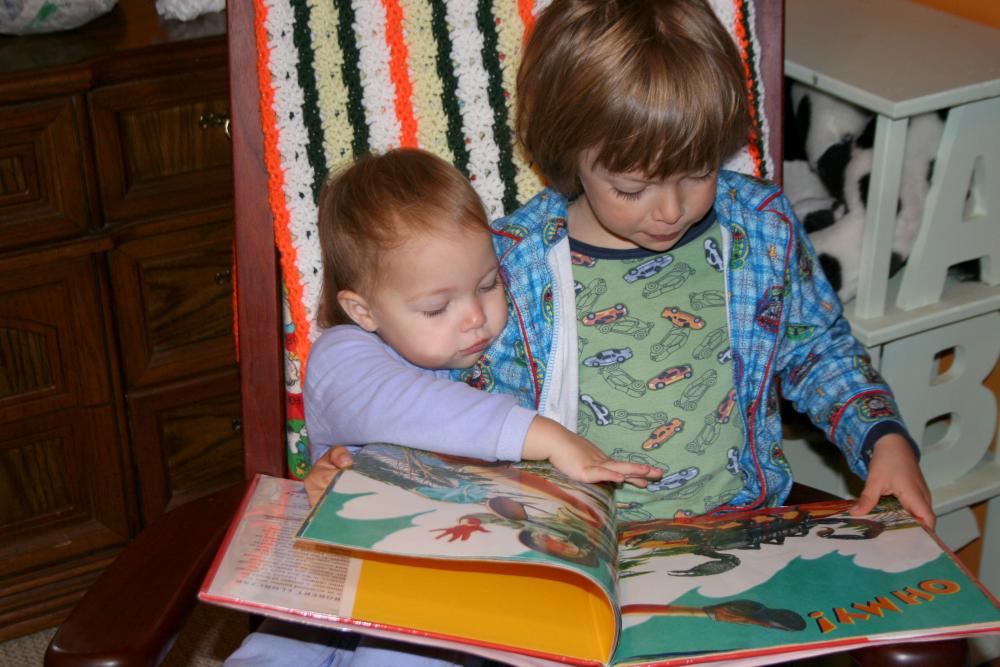 Baby Raven and a young Micah sit together reading a book.