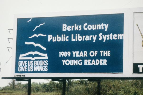 Stick birds flying from book icon on Berks County Public Libraries blue billboard